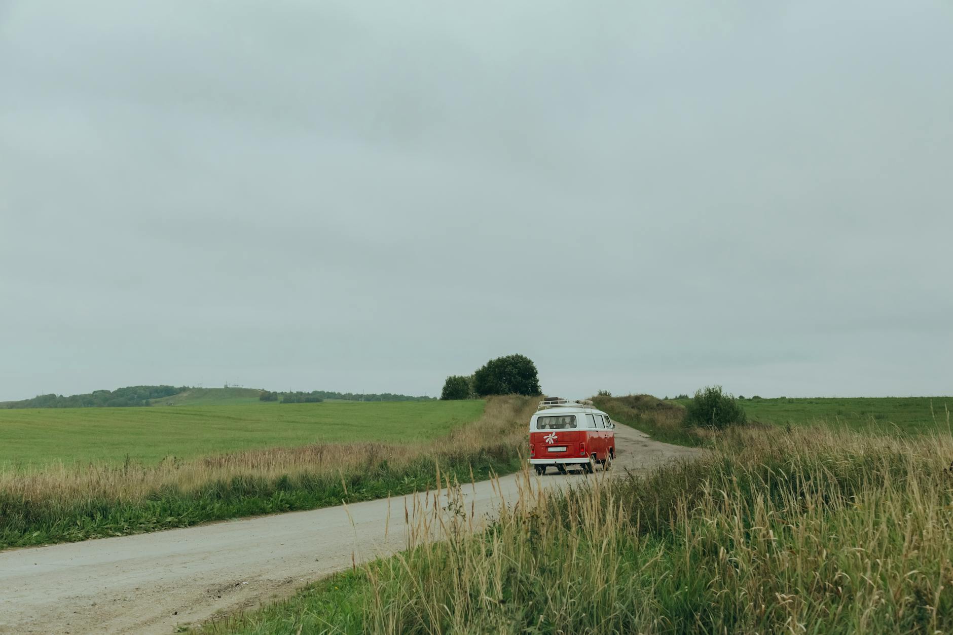 Czerwony bus jedzie wiejską drogą pod zachmurzonym niebem