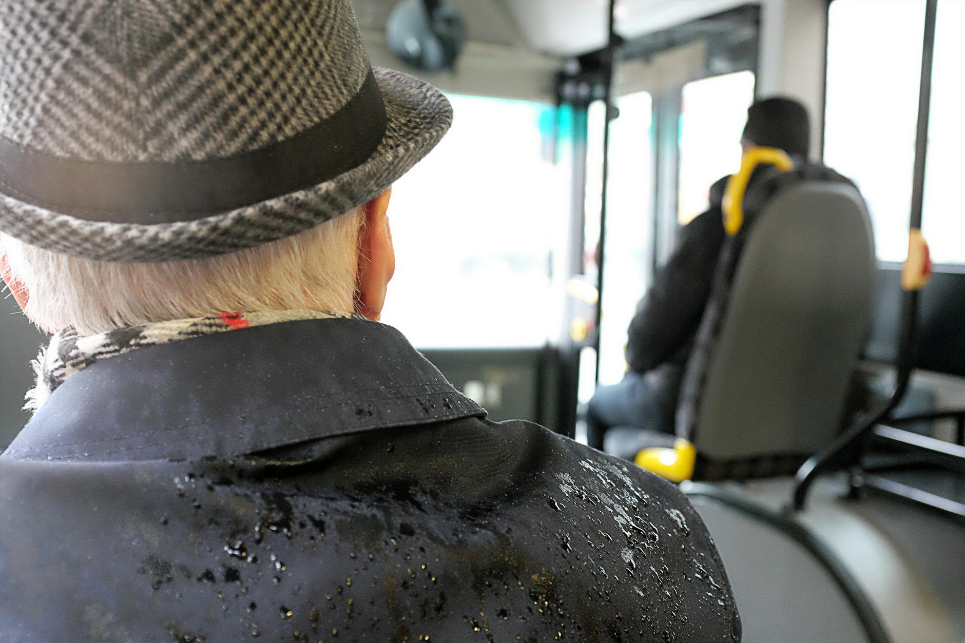 Starszy mężczyzna w kapeluszu patrzy przez okno autobusu w deszczową pogodę Starszy mężczyzna w kapeluszu patrzy przez okno autobusu w deszczową pogodę