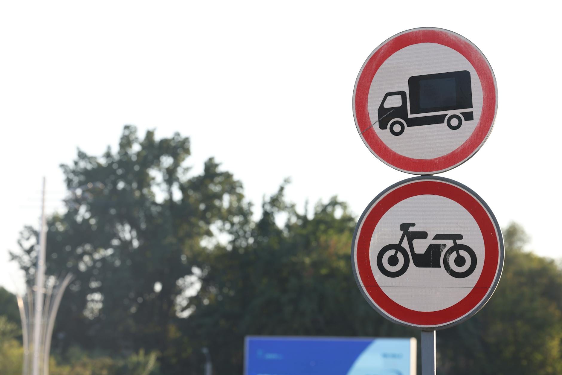 Znaki zakazu dla ciężarówek i motocykli na tle drzew