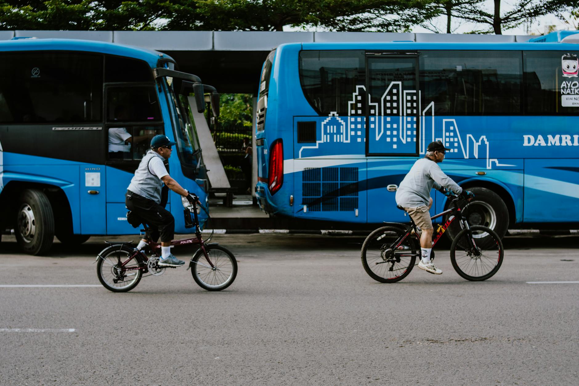 Dwaj rowerzyści jadą obok zaparkowanych busów na miejskiej ulicy