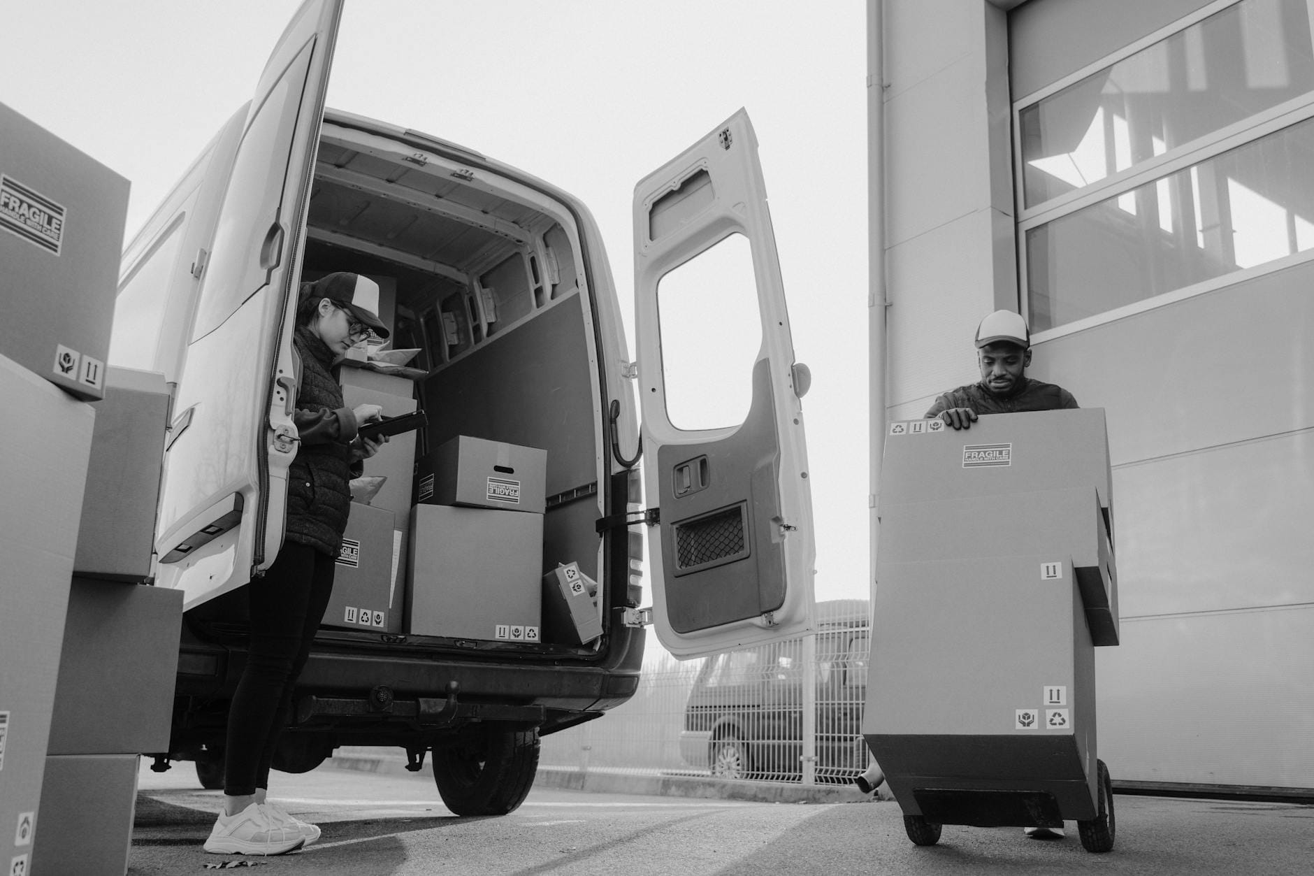 Pracownicy rozładowują paczki z busa na wózek w centrum logistycznym