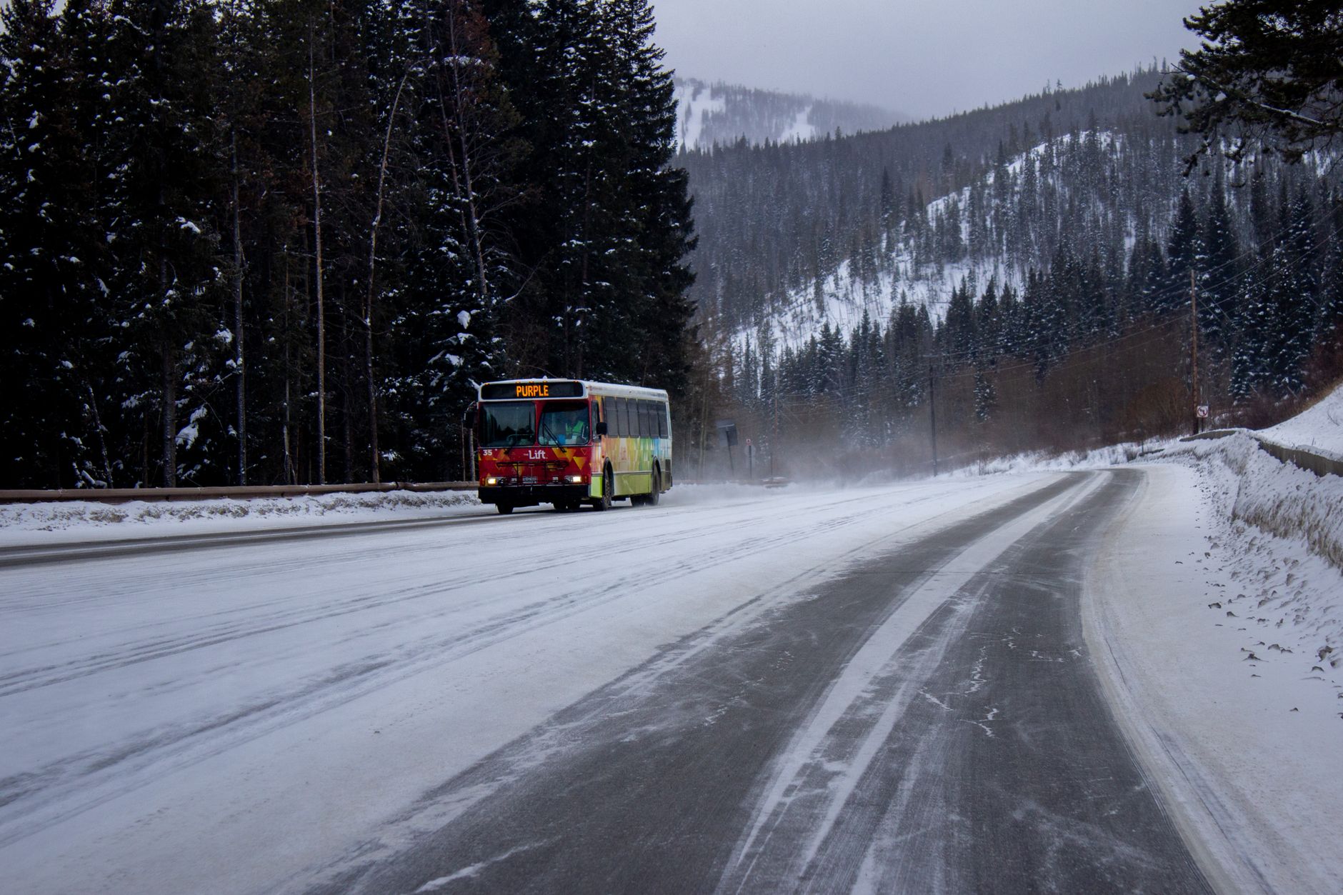 Kolorowy bus jedzie ośnieżoną drogą w górach zimą